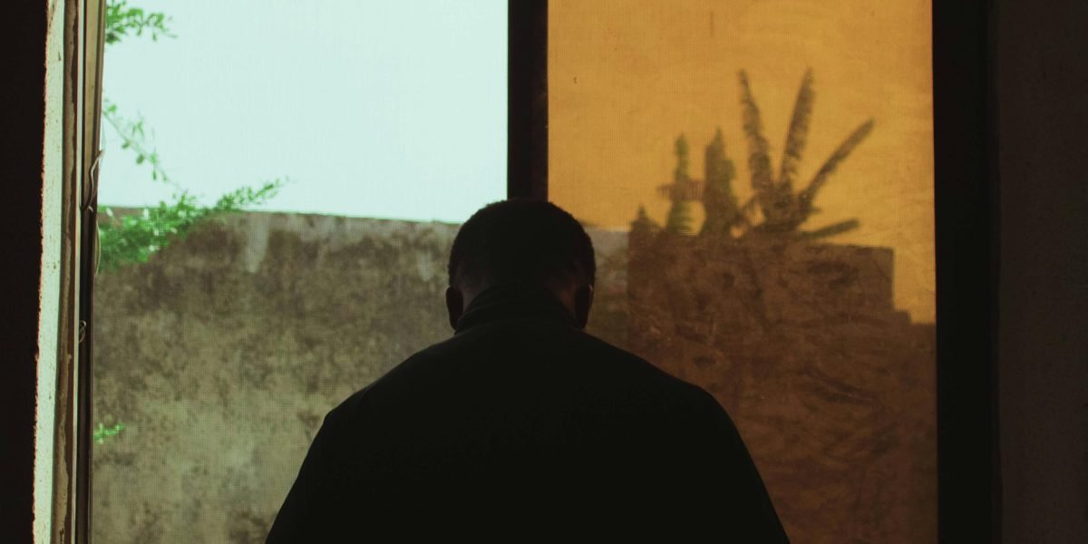 A thoughtful man looks out a window, reflecting the quiet struggle of male loneliness discussed in the article.